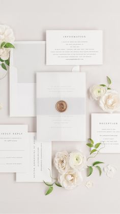 the wedding stationery is laid out on top of each other with white flowers and greenery