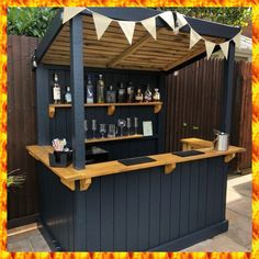 an outdoor bar with bottles and glasses on the top shelf in front of a fence