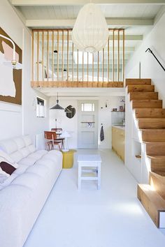 a living room filled with white furniture and wooden steps leading up to the second floor