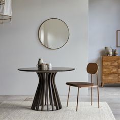 a dining table with two chairs and a round mirror on the wall above it in a white room