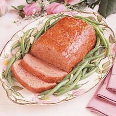 a loaf of bread on a plate with green beans and pink flowers in the background