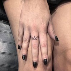 a woman's hand with a small crown tattoo on her left ring and black nail polish