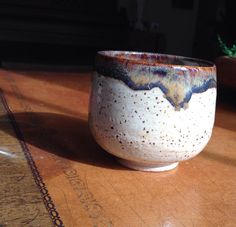 a white and blue cup sitting on top of a wooden table next to a potted plant