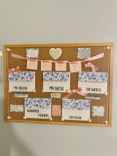 a cork board that has some paper on it and pink ribbon hanging from the pegs