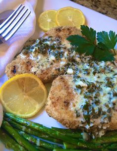 a white plate topped with chicken, asparagus and lemon slices next to a fork