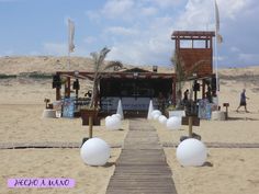 a wooden walkway leading to an open air bar on the beach with white balls and palm trees