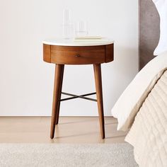 a small table with two glasses on it next to a bed