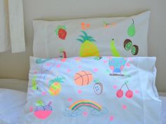 a white bed topped with lots of pillows covered in fruit and veggie designs