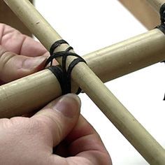 two hands are working on an object made out of bamboo sticks and black leather cords