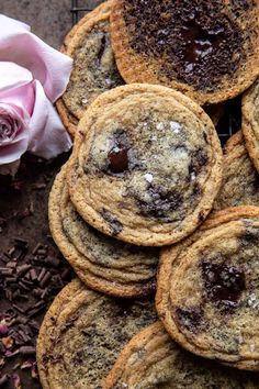 chocolate chip cookies are piled on top of each other next to a pink rose and some sprinkles