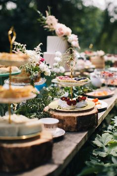 a table filled with cakes and desserts on top of wooden boards surrounded by greenery