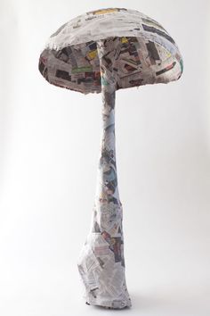 a mushroom made out of newspaper sitting on top of a white table next to a lamp