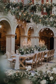 an indoor wedding venue with white flowers and greenery on the tables, chandeliers and candles