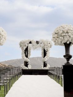 an outdoor ceremony set up with white flowers and black vases on the sidelines