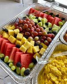 an assortment of fruits and cheeses in trays on a table with wine glasses