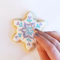 a hand holding a cookie decorated like a snowflake with blue and purple designs