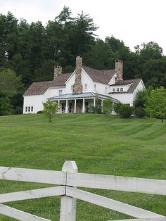 a large white house sitting on top of a lush green field next to a forest