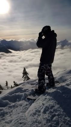 a man standing on top of a snow covered slope next to the sun and clouds