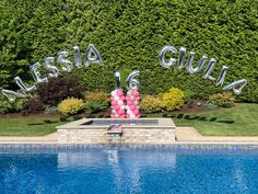 a pool with some balloons in the shape of letters and numbers next to it is surrounded by greenery