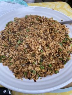 a white plate topped with fried rice and green onions next to a fork on a yellow table cloth