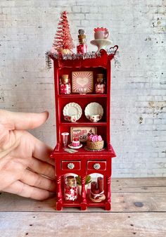 a hand is holding a miniature red china cabinet