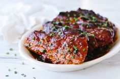 a white bowl filled with meat covered in sauce and garnished with parsley