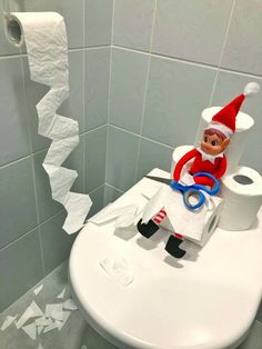 an elf sitting on top of a toilet in a bathroom next to a roll of toilet paper