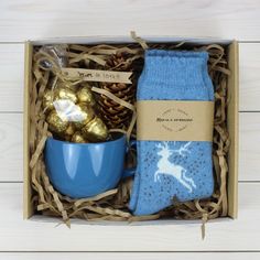 an open box containing socks, chocolates and a cup with gold foil in it