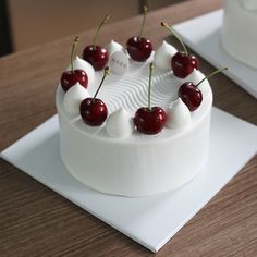 a white cake with cherries on it sitting on a table next to another plate