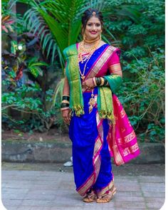 a woman in a blue and pink sari standing on a brick walkway with greenery behind her