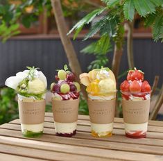 three cups filled with different types of desserts on top of a wooden table next to a tree