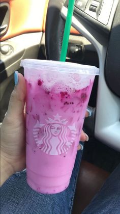 a person holding up a pink drink in their hand while sitting in the drivers seat