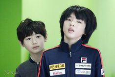 two young boys standing next to each other in front of a green wall with stickers on them