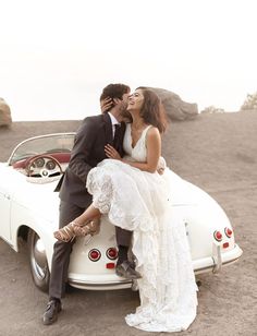 a bride and groom sitting on the back of a white convertible car in the desert