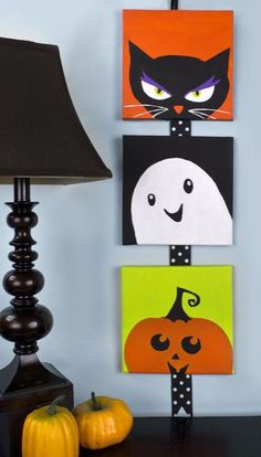 three halloween paintings are hanging on the wall next to a black lamp and two pumpkins