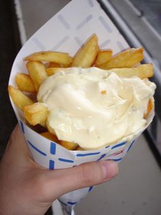 a hand holding a paper container filled with french fries covered in mayonnaise and ketchup