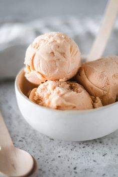 three scoops of ice cream in a white bowl on a marble surface with spoons