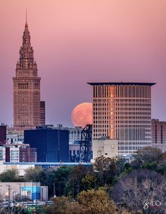 the full moon is setting behind some tall buildings