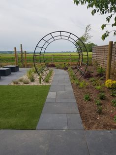 an outdoor garden with grass, flowers and plants on the side walk way in front of a wooden fence