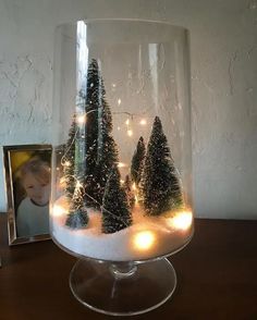 a glass vase filled with snow covered trees and lights on top of a wooden table