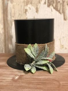 a black top hat with green leaves and burlock on the front, sitting on a wooden table