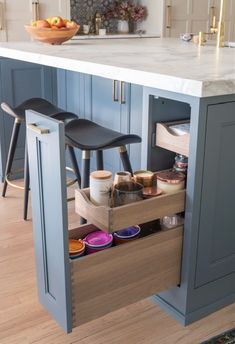 an open cabinet in a kitchen with stools and bowls on the bottom shelf next to it