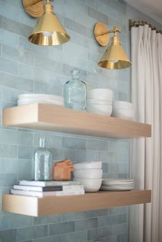 two brass light fixtures hang above shelves in a kitchen with blue tile walls and white curtains