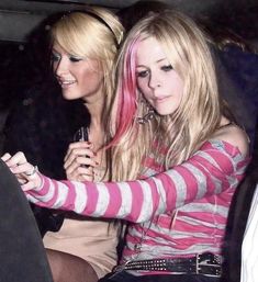 two women sitting in the back seat of a car, one with pink hair looking at her cell phone