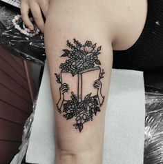 a woman with a tattoo on her arm holding a box filled with flowers and leaves