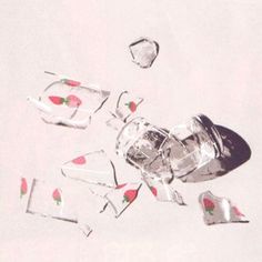 broken glass pieces with strawberries and ice cubes scattered around them on a white surface