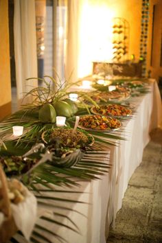 a long table with lots of food on it and palm fronds in the middle