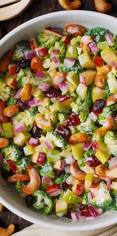 a white bowl filled with broccoli, apples, raisins and nuts