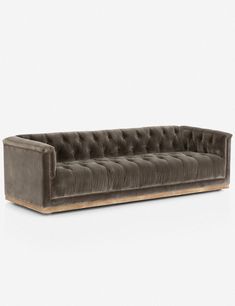 a gray velvet couch with wooden legs and buttons on the back, in front of a white background