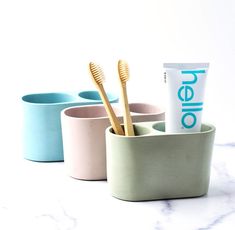 three cups with toothbrushes in them sitting on a marble counter next to a tube of toothpaste